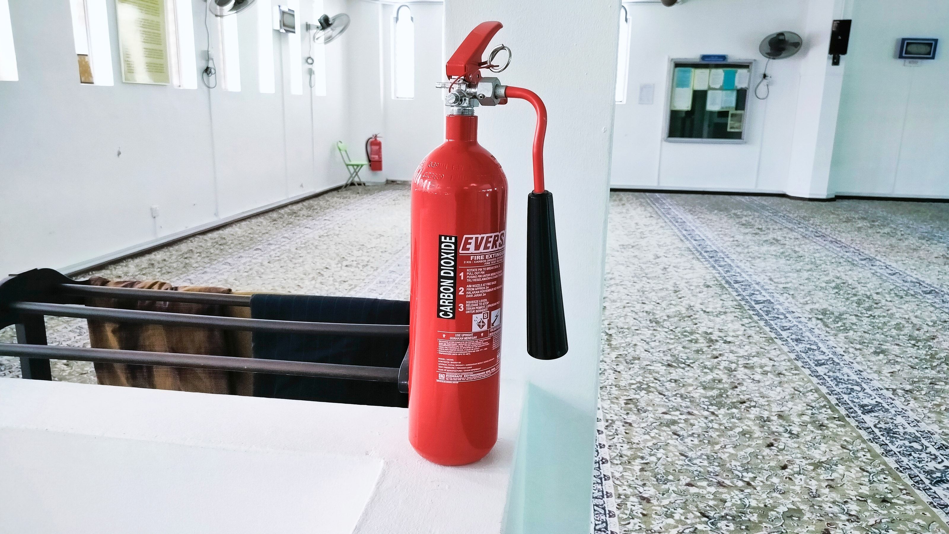 Extintor de polvo químico ABC sobre soporte de pared en una instalación industrial, con etiqueta visible de las clases de fuego A, B y C