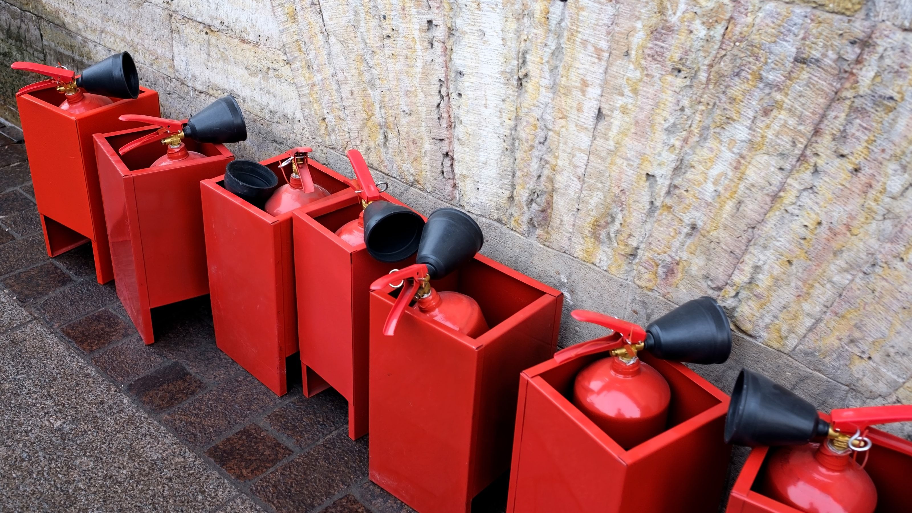 Varios extintores portátiles rojos alineados en un entorno industrial, representando los diferentes tipos según agente extintor